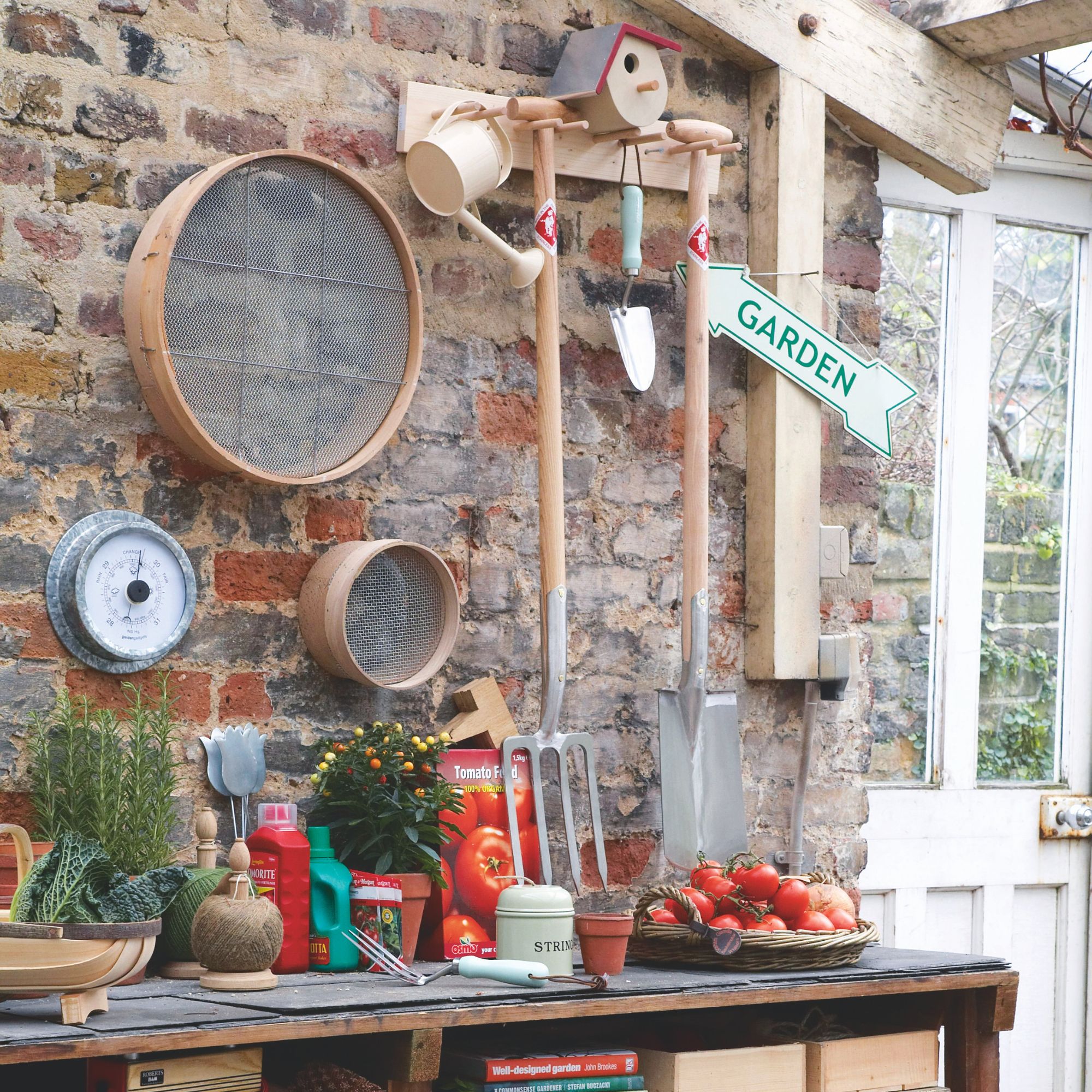 Garden spade and fork hanging against brick wall above potting bench