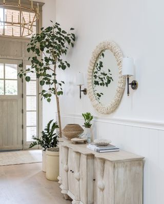 white hallway with whitewashed cabinet, round mirror and gold chandelier