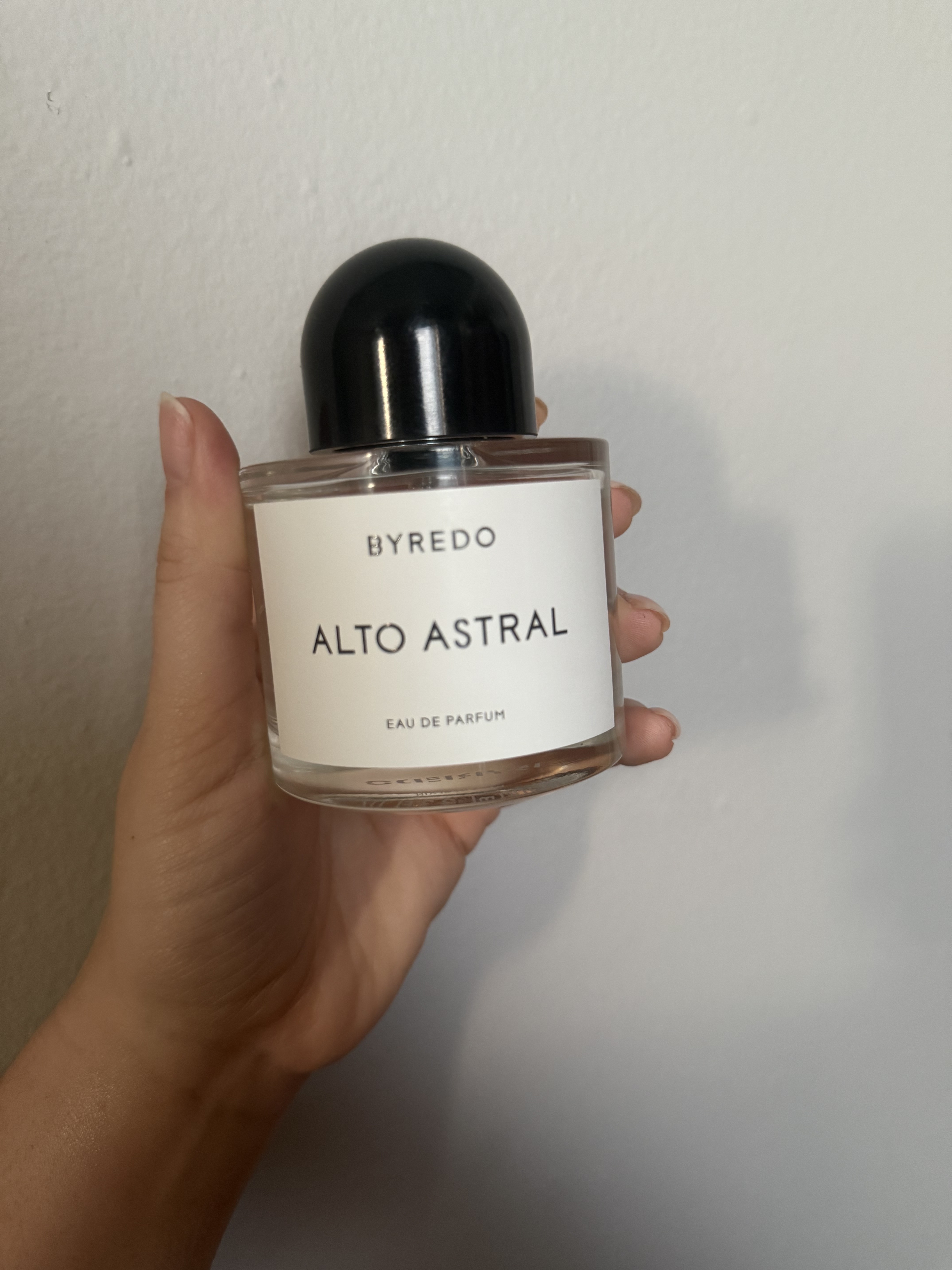 Brooke Knappenberger holds up Byredo Alto Astral perfume against grey wall