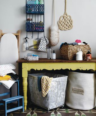 A modern traditional laundry room with linen laundry baskets, wooden table painted with neon yellow paint and an assortment of cleaning equipment