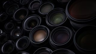 A wide collection of Fujifilm lenses, illuminated with low key lighting, on a black background
