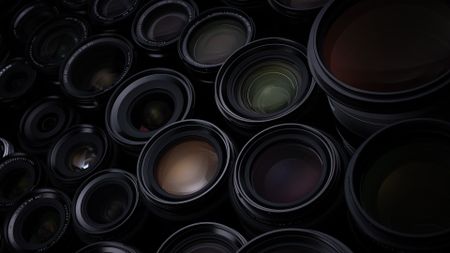 A wide collection of Fujifilm lenses, illuminated with low key lighting, on a black background