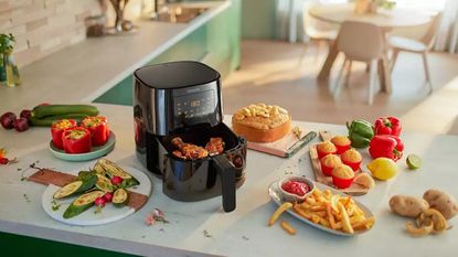 Philips Essential Air Fryer on kitchen countertop surrounded by assortment of cooked food items