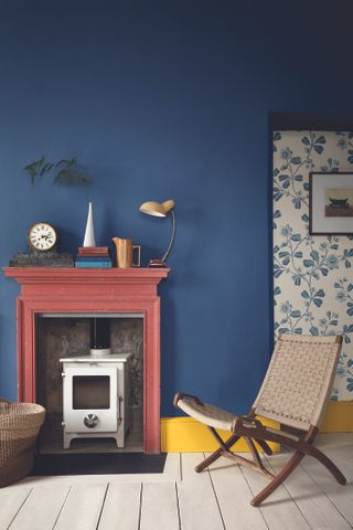 blue living room with painted dark pink fire surround, small white log burner, white floors, blue wallpaper, yellow skirtings