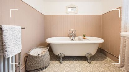 a freestanding white bathtub in a cute bathroom, with pink panelled walls, a laundry basket, artwork, and a radiator with a towel on it, to illustrate how to clean a bathtub