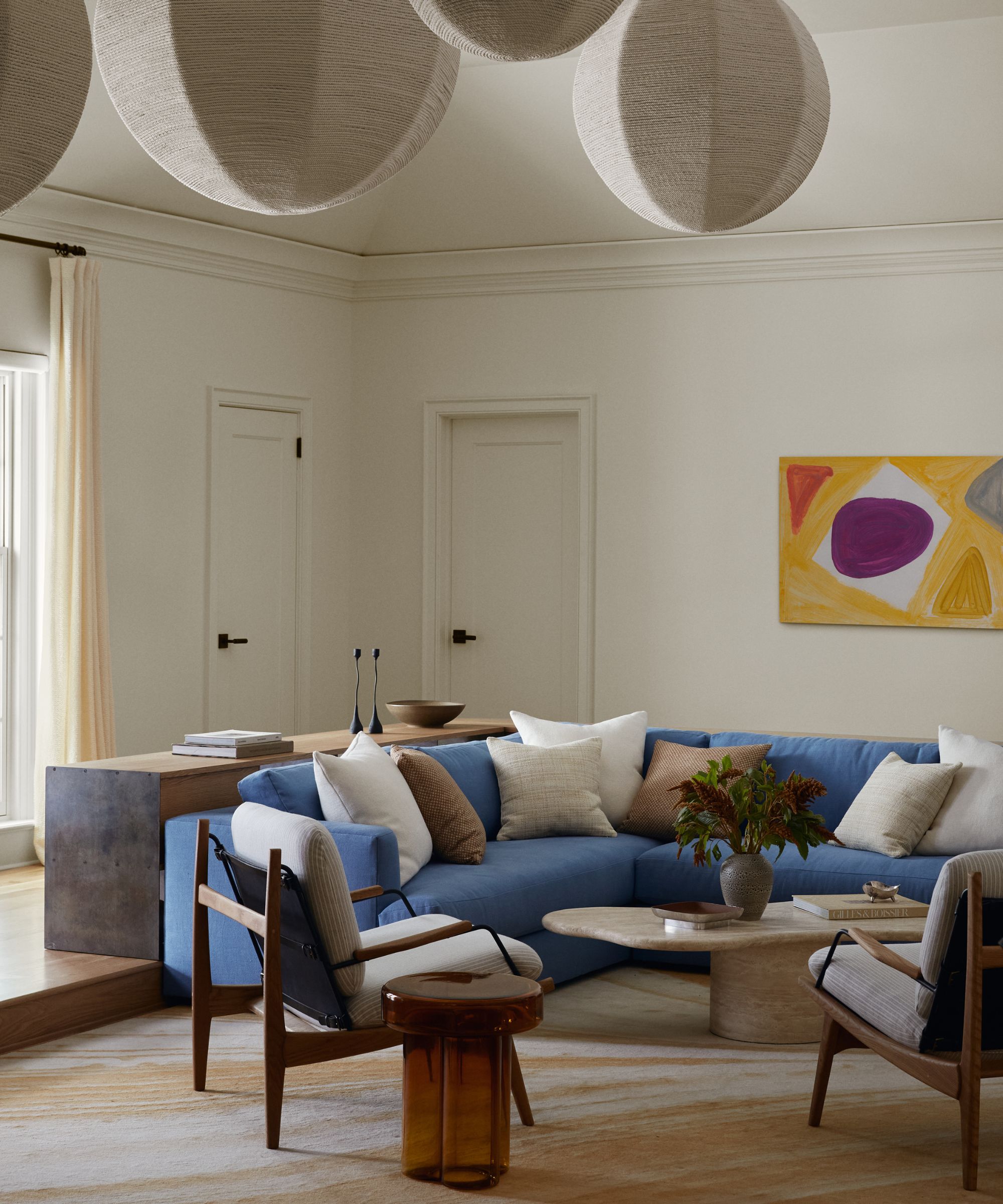 White living room with large blue corner couch, stone coffee table and two beige and wooden armchairs
