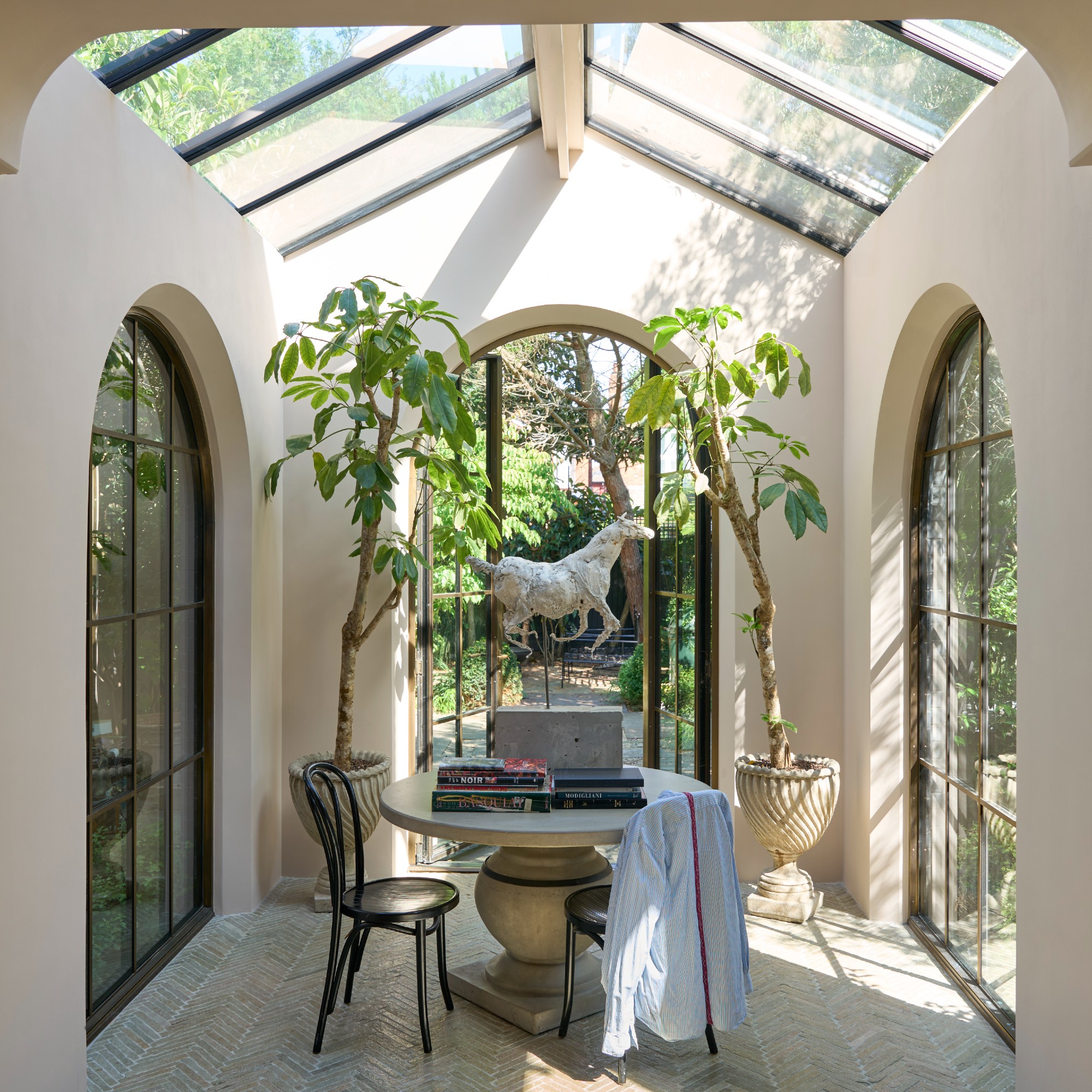 A winter garden with curved windows in Farrow & Ball -Jakobschussel, decorated with a round table in the middle and two bistro chairs