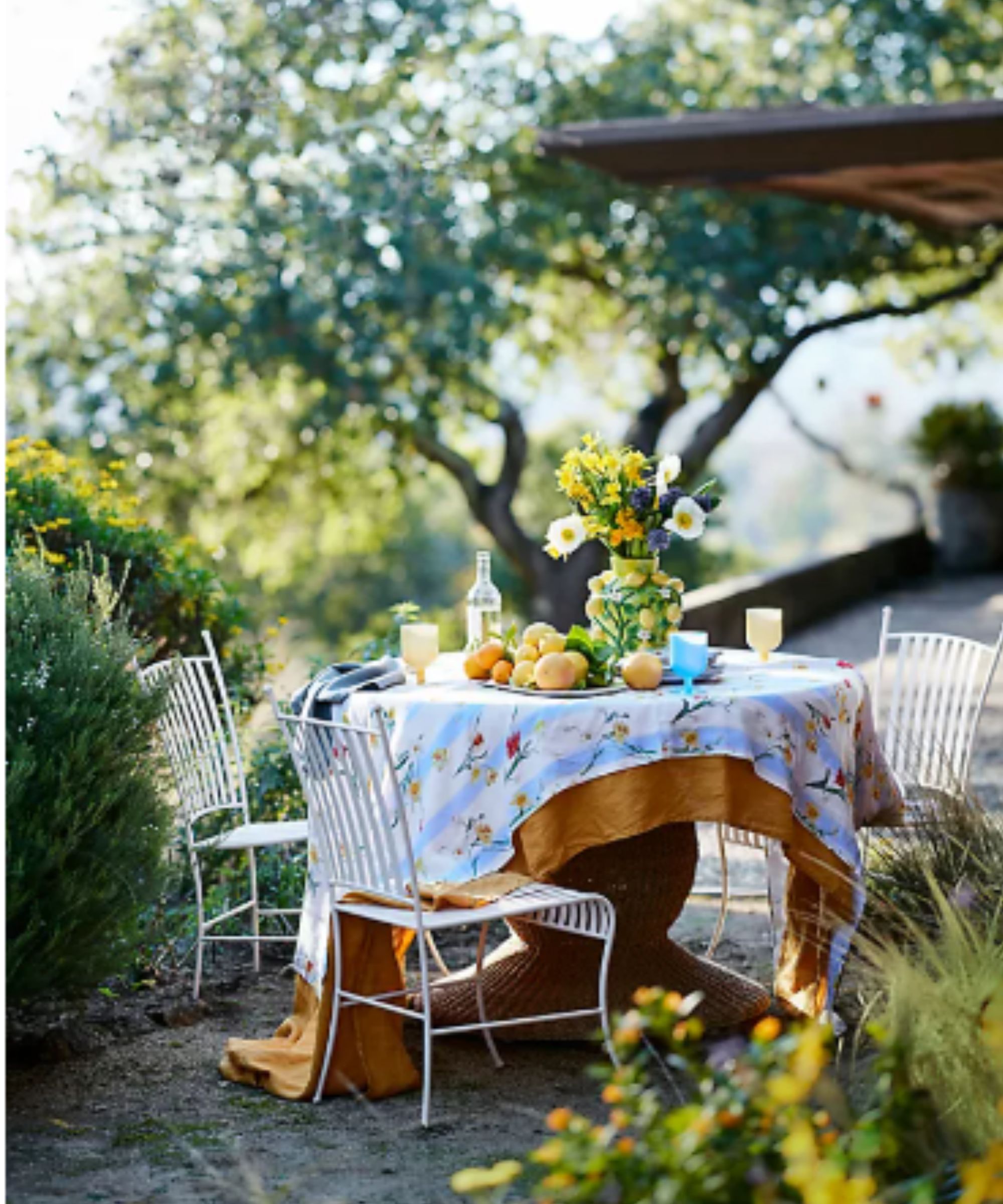 Terrain Mediterranean tablescape with linen table cloths and a lemon vase filled with summer flowers