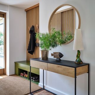 A bright and modern hallway with a panelled wall section with a contrasting green show bench