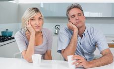 Portrait of a bored couple sitting with coffee cups in the kitchen at home
