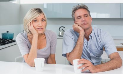 Portrait of a bored couple sitting with coffee cups in the kitchen at home