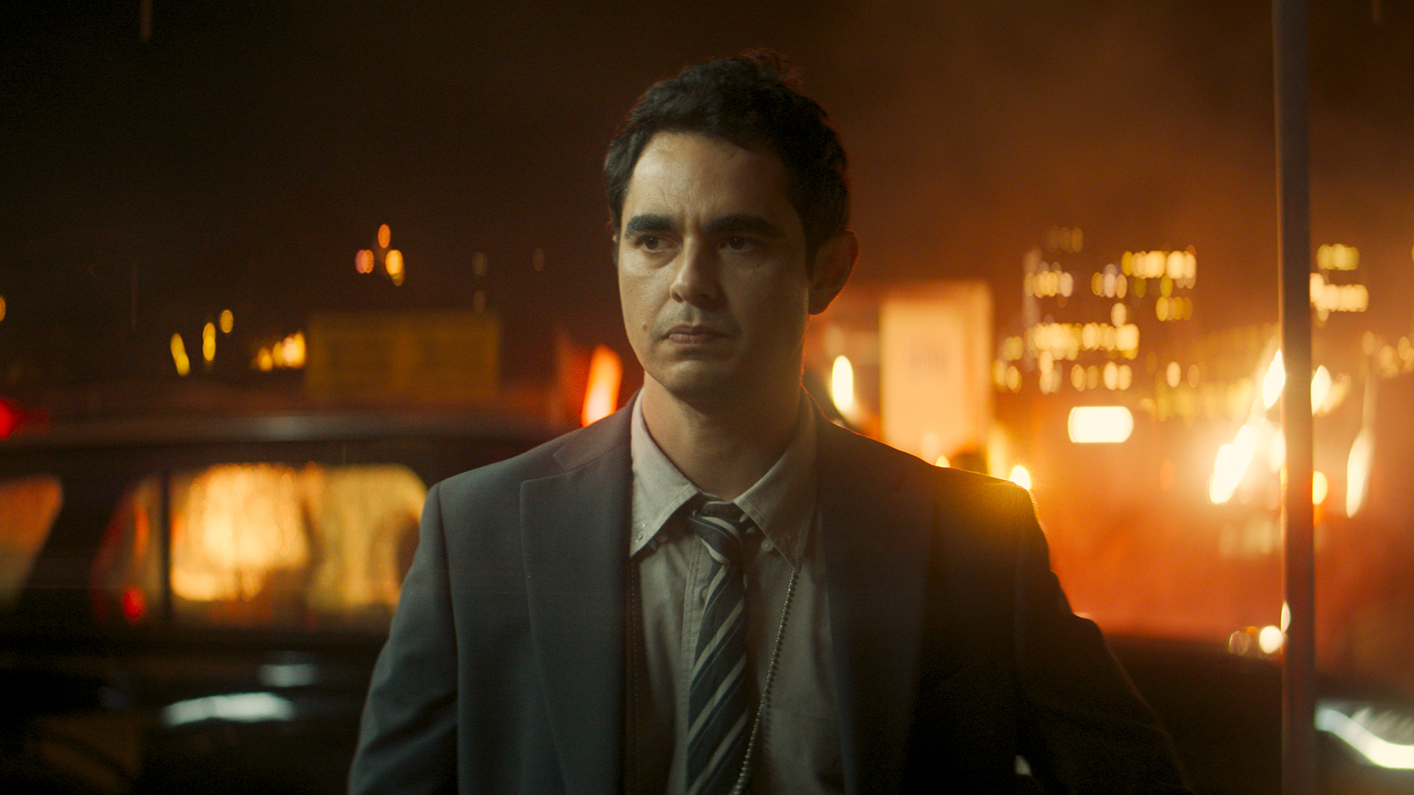 Max Minghella's John Borelli standing in a street at night in Clayface