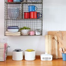 Ceramic storage jars and a ceramic butter dish sitting on a wooden kitchen worktop next to two propped up wooden chopping boards and below a wire wall shelf