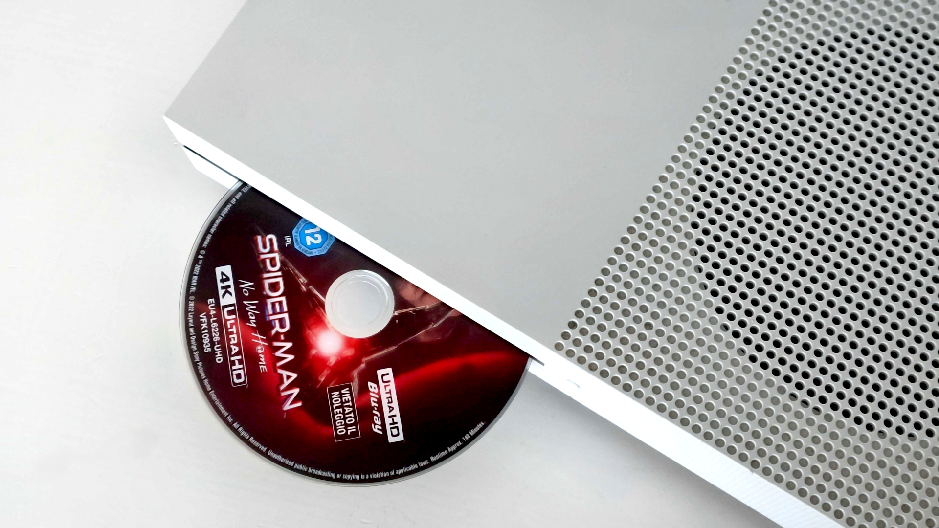 The white Xbox One S console pictured from the top with a 4K UHD Blu-Ray of Spider-Man: No Way Home ejected from the disc drive. 