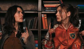 Lena Headey and Karen Gillan prepare their guns behind a bookcase in Gunpowder Milkshake.