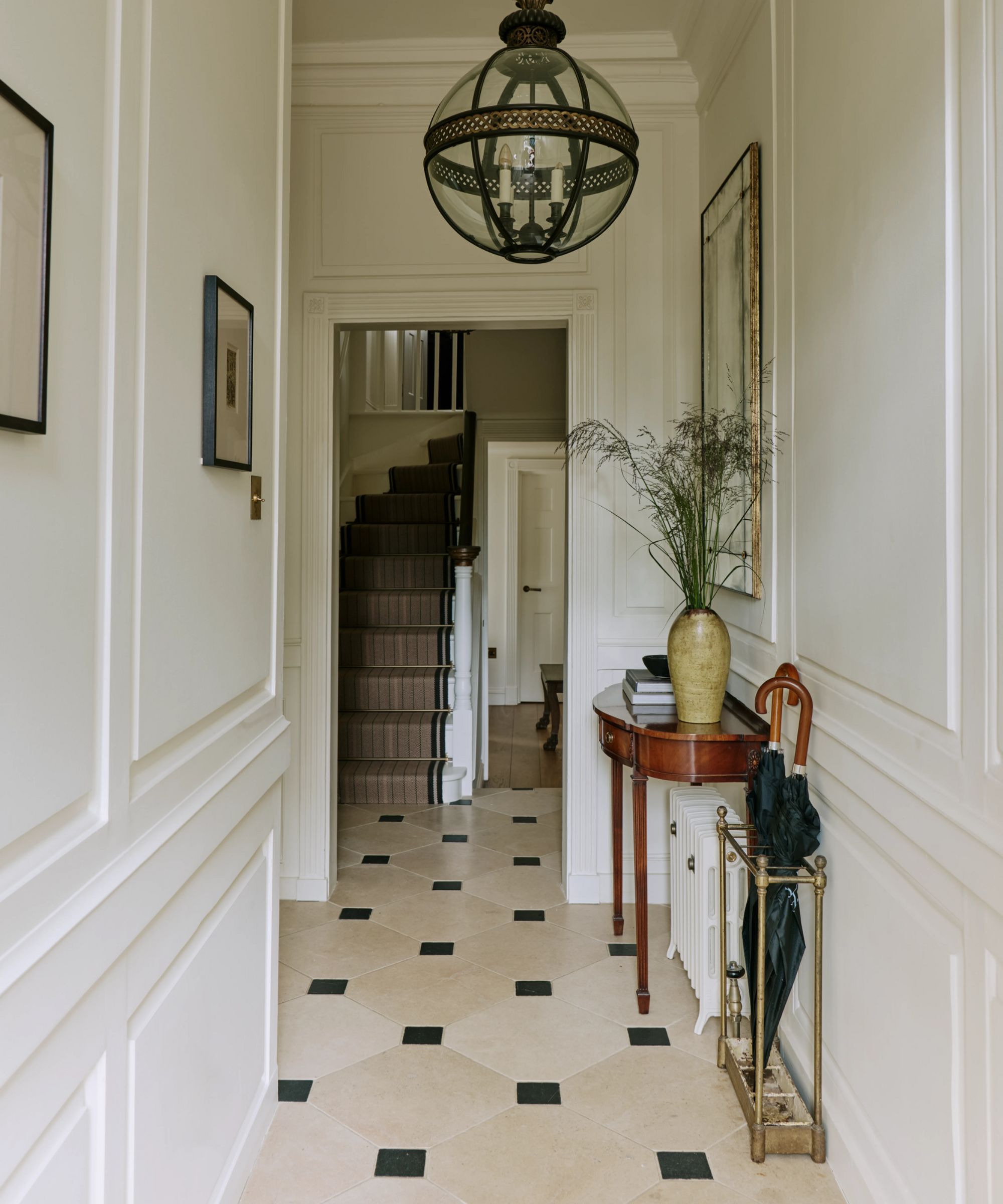 a narrow entryway in a london townhouse with stone flooring, wall paneling, large antique globe pendant and an antique hall table