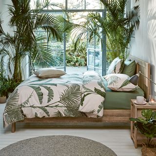 bedroom with wooden bed green and white cushion plants and white wooden flooring