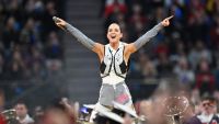 Singer Katy Perry points with arms raised pointing to a crowd over a marching band