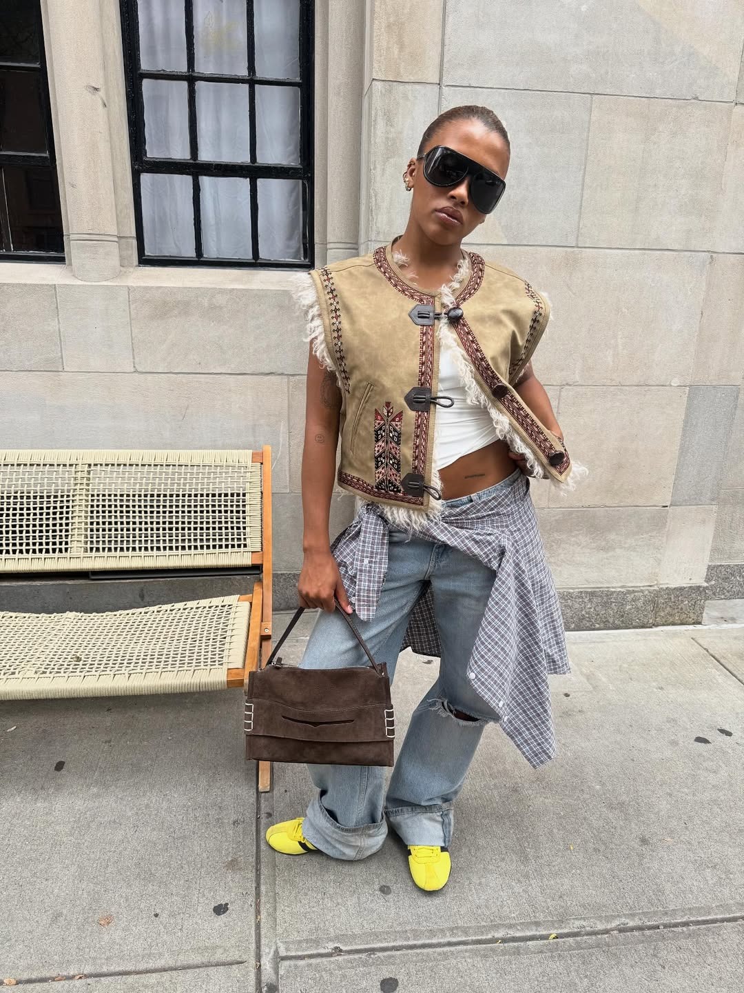 @mv.tianguew wearing jeans, Adidas sneaker, suede shoulder bag, frog-closure vest, and sunglasses