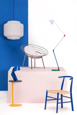 A selection of furniture in a studio including a blue chair, a yellow side table, and a large angle-poised lamp in different colours