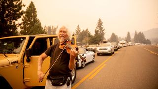 A man plays the violin as evacuees are stuck in traffic as they flee the fires.
