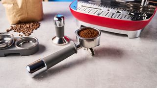 a red smeg espresso machine with burr grinder is photographed against a blue background