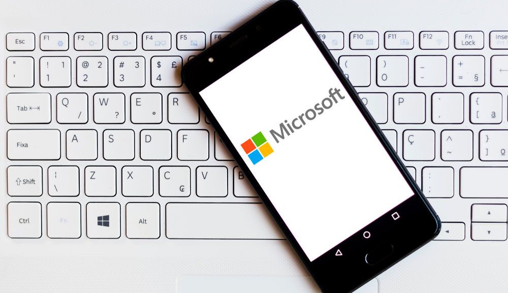 Microsoft logo displayed on an Android smartphone resting on the keyboard of a Windows laptop.