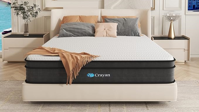 The Crayan Mattress on a low bed frame in a bedroom. The mattress has a white quilted top, gray side paneling and the Crayan logo on the front of the mattress