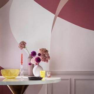 Pink colored wall and a white coffee table with pink vases and flowers topped with contrasting colored accessories