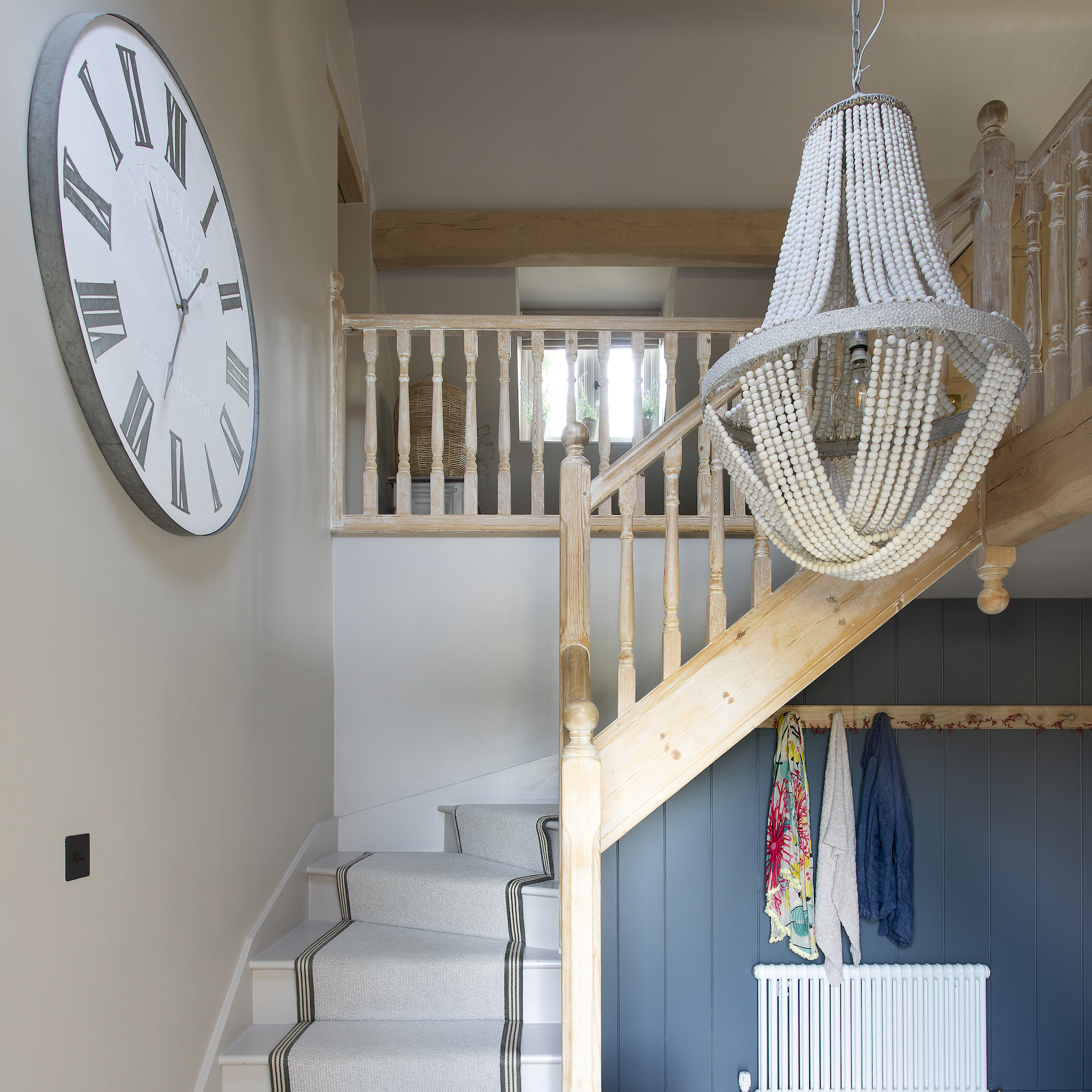 stairway with wooden bannister, pale runner carpet, cream bead chandelier and large wall clock