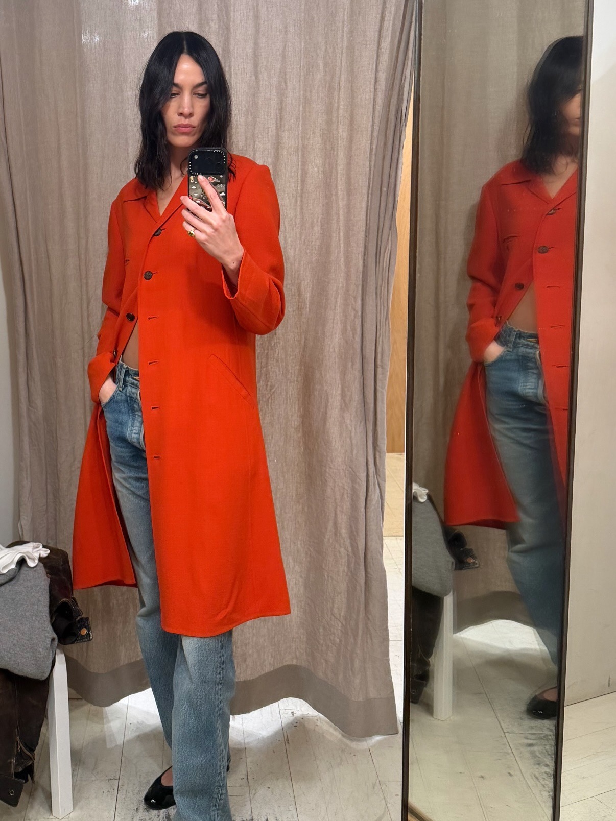Alexa Chung takes a mirror selfie wearing a tomato red jacket with blue jeans and black ballet flats.