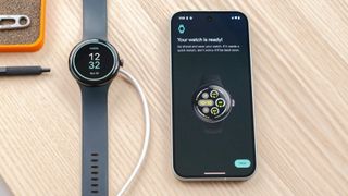 Google Pixel Watch 3 on a wood table next to a Pixel 9 smartphone showing a screen saying the new watch setup is complete