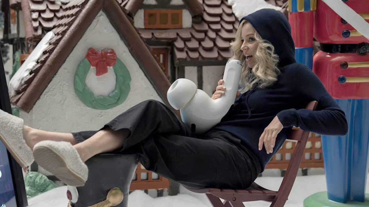 Elizabeth Banks in a hoodie talking on an airpod in The Miniature Wife