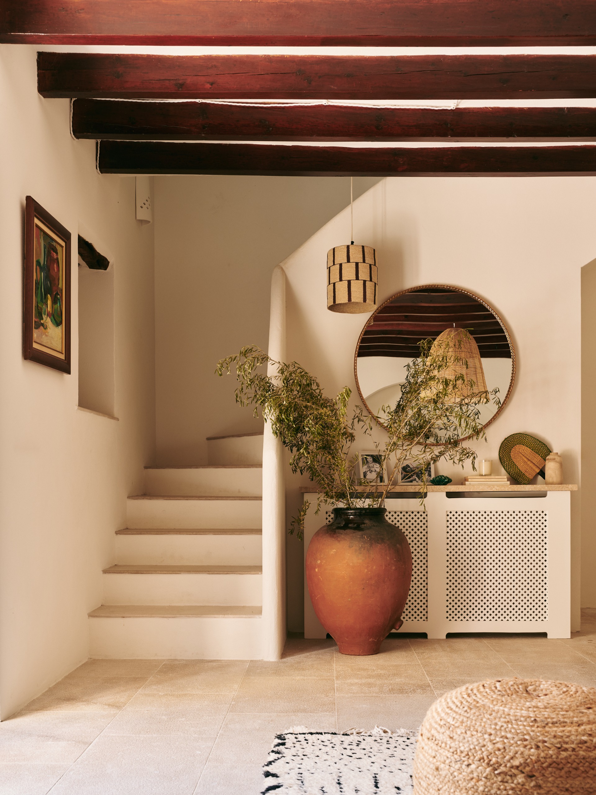 a white plaster, rounded staircase in a white-washed home with wooden beams in the ceiling and a large potted plant to the side