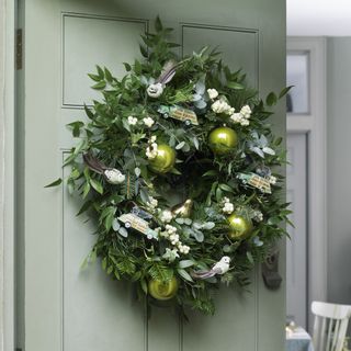 Fresh Christmas Wreath dotted with fun decoartions on a pale green door