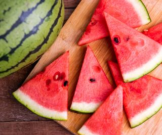 Triangular slices of watermelon on a cutting board next to a whole watermelon