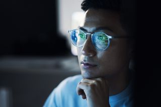 Close up shot of a male cyber security analyst looking at a computer screen in dimly lit room.