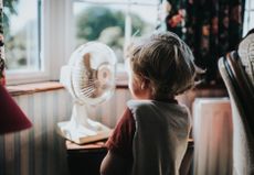 A picture of a young child standing in front of a small electric fan