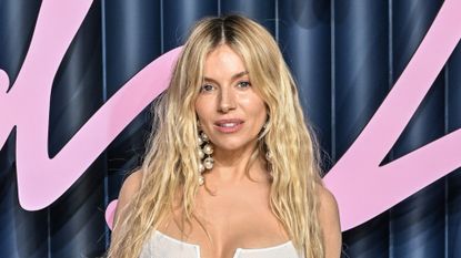 Sienna Miller is pictured with wavy hair and wearing large pearl earrings and a white dress at The Fashion Awards 2025 held at Royal Albert Hall on December 01, 2025 in London, England.