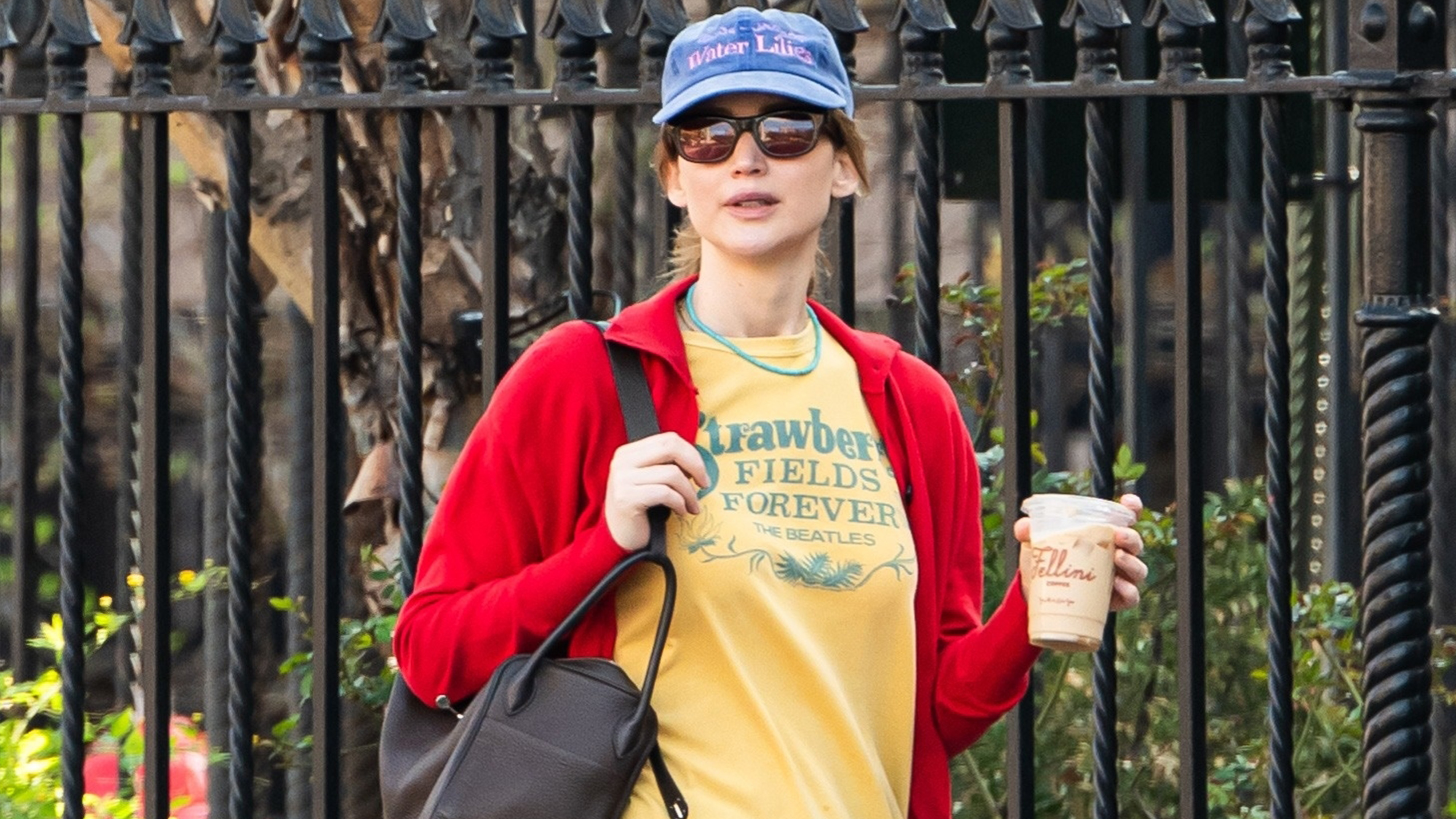 Jennifer Lawerence wears a blue baseball cap, red shirt, yellow graphic tee, and baggy jeans.
