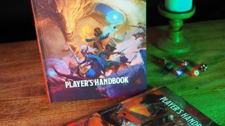 Dungeons &amp; Dragons Player&#039;s Handbook standing on a wooden table beside dice, a candle, and the 2014 Player&#039;s Handbook