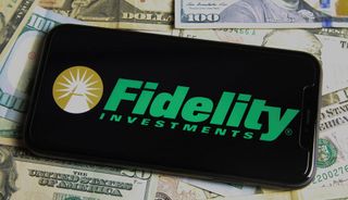 A phone with the Fidelity Investments logo seen on a bed of $100 bills. 