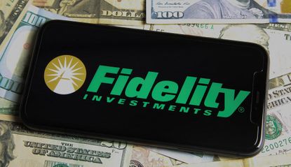 A phone with the Fidelity Investments logo seen on a bed of $100 bills. 