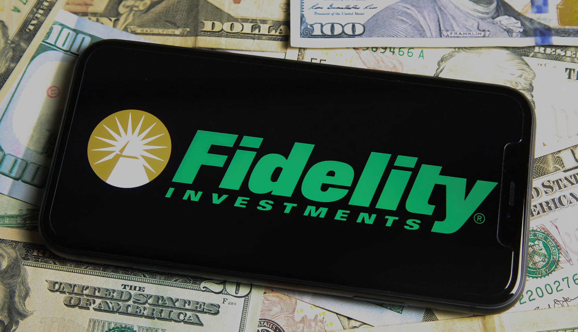 A phone with the Fidelity Investments logo seen on a bed of $100 bills. 