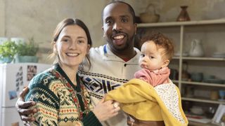 Charlotte Ritchie in a festive cardigan as Alison and Kiell Smith-Bynoe in a Christmas jumper as Mike hold a baby in the Ghosts Christmas special.
