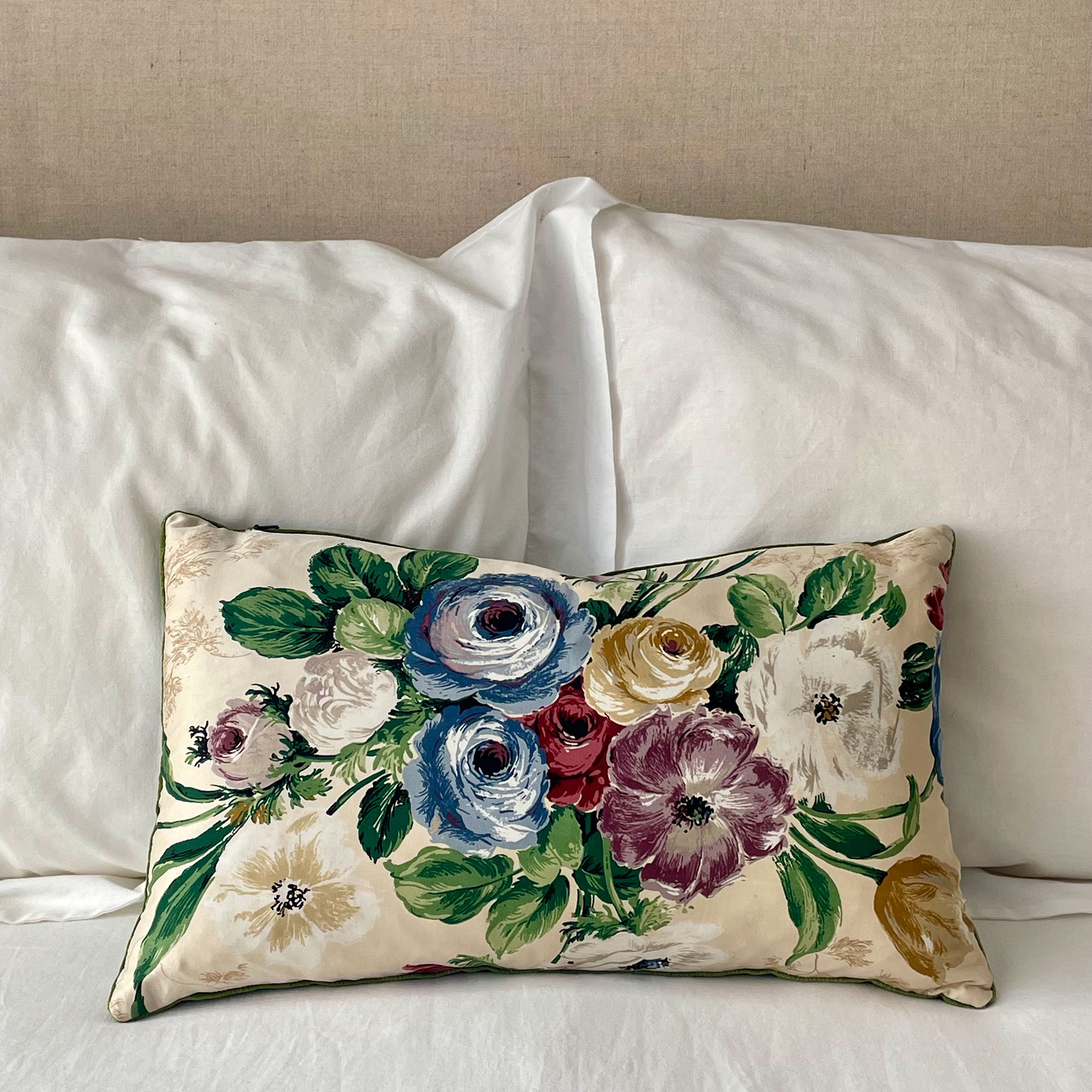 Floral print cushion sitting on bed with white linens