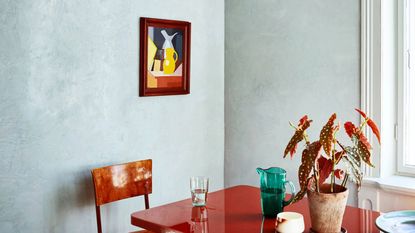 Dining room painted in a pale shade of mineral blue with a red table and spotted houseplant