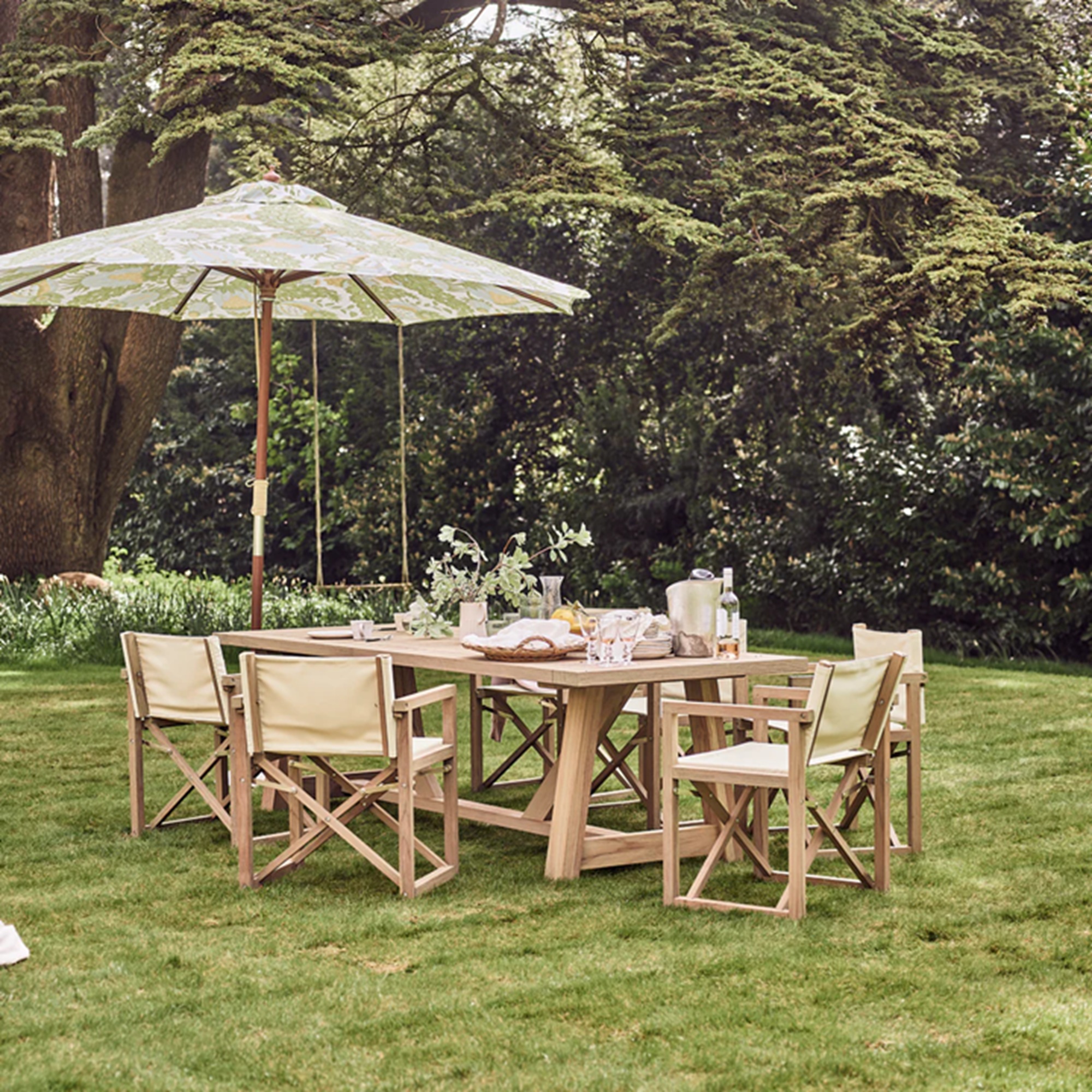 a teak outdoor table set with a green umbrella above on a lawn