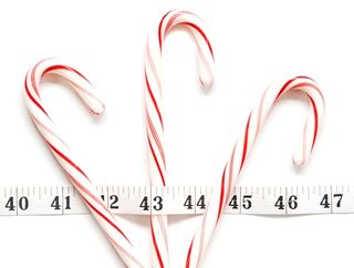 Candy canes sit on a table with a measuring tape over them.