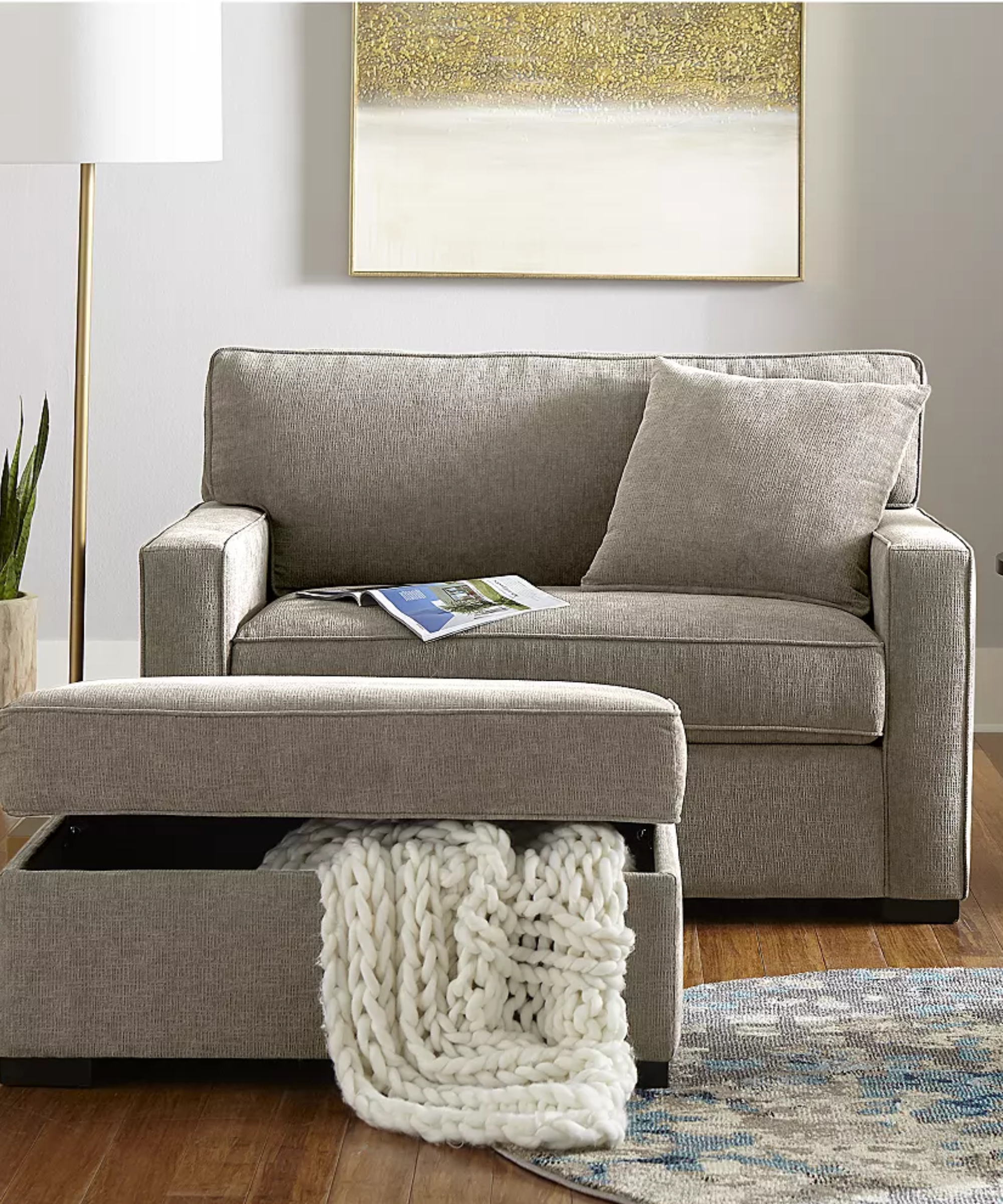 Macy's chair sofa bed pictured in a neutral living room alongside a coordinating storage ottoman, floor lamp, and a colorful accent rug